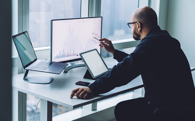 Młody mężczyzna przed kompuetrem ma otwartą stronę przedstawiającą wykresy inwestycji.