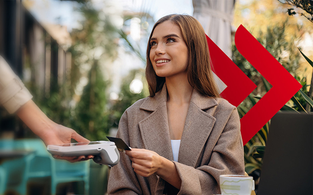 Młoda, uśmiechnięta kobieta płacąca kartą bankową w kawiarni.